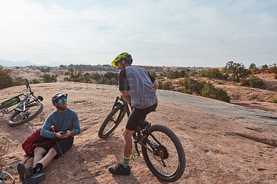 Buy stock photo Full length shot of two athletic men taking a break while mountain biking through the wilderness