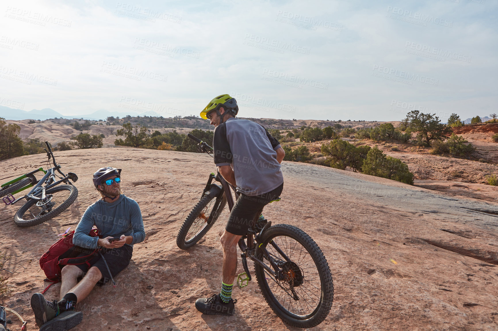 Buy stock photo Full length shot of two athletic men taking a break while mountain biking through the wilderness