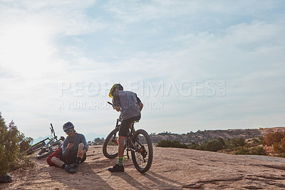 Buy stock photo Full length shot of two athletic men taking a break while mountain biking through the wilderness