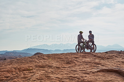 Buy stock photo Full length shot of two athletic men taking a break to admire the view while mountain biking through the wilderness