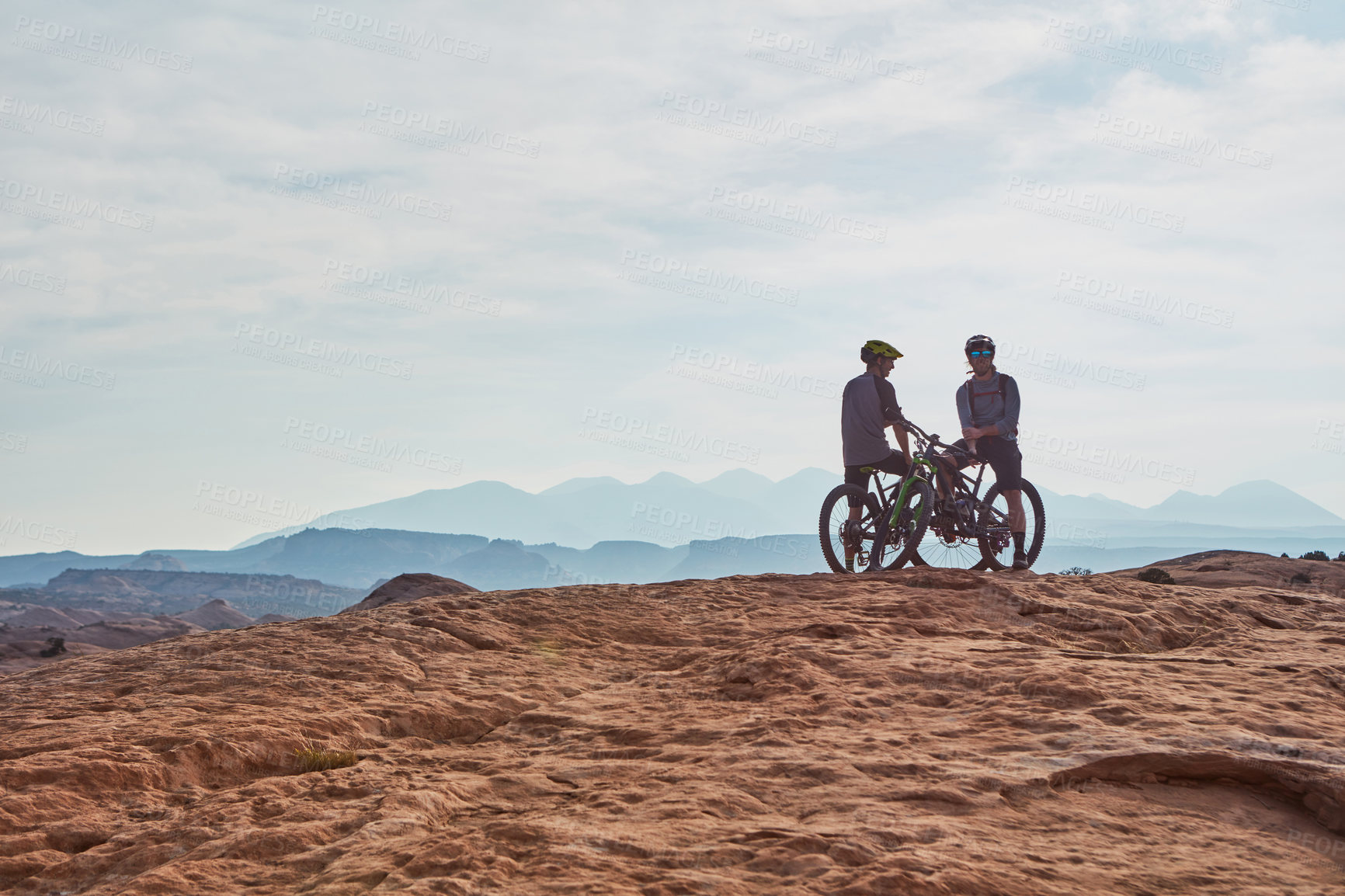 Buy stock photo Full length shot of two athletic men taking a break to admire the view while mountain biking through the wilderness