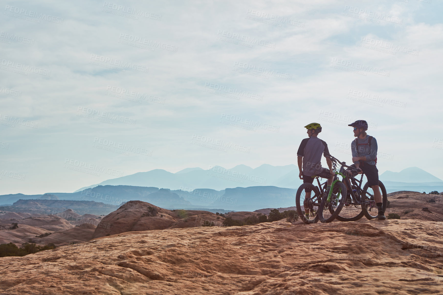 Buy stock photo Full length shot of two athletic men taking a break to admire the view while mountain biking through the wilderness