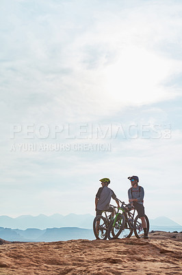 Buy stock photo Full length shot of two athletic men taking a break to admire the view while mountain biking through the wilderness