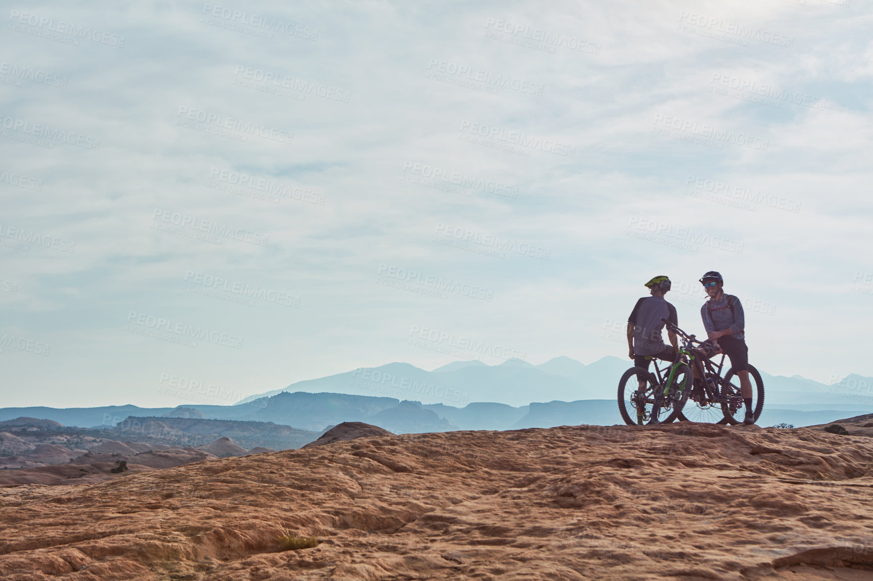 Buy stock photo Full length shot of two athletic men taking a break to admire the view while mountain biking through the wilderness