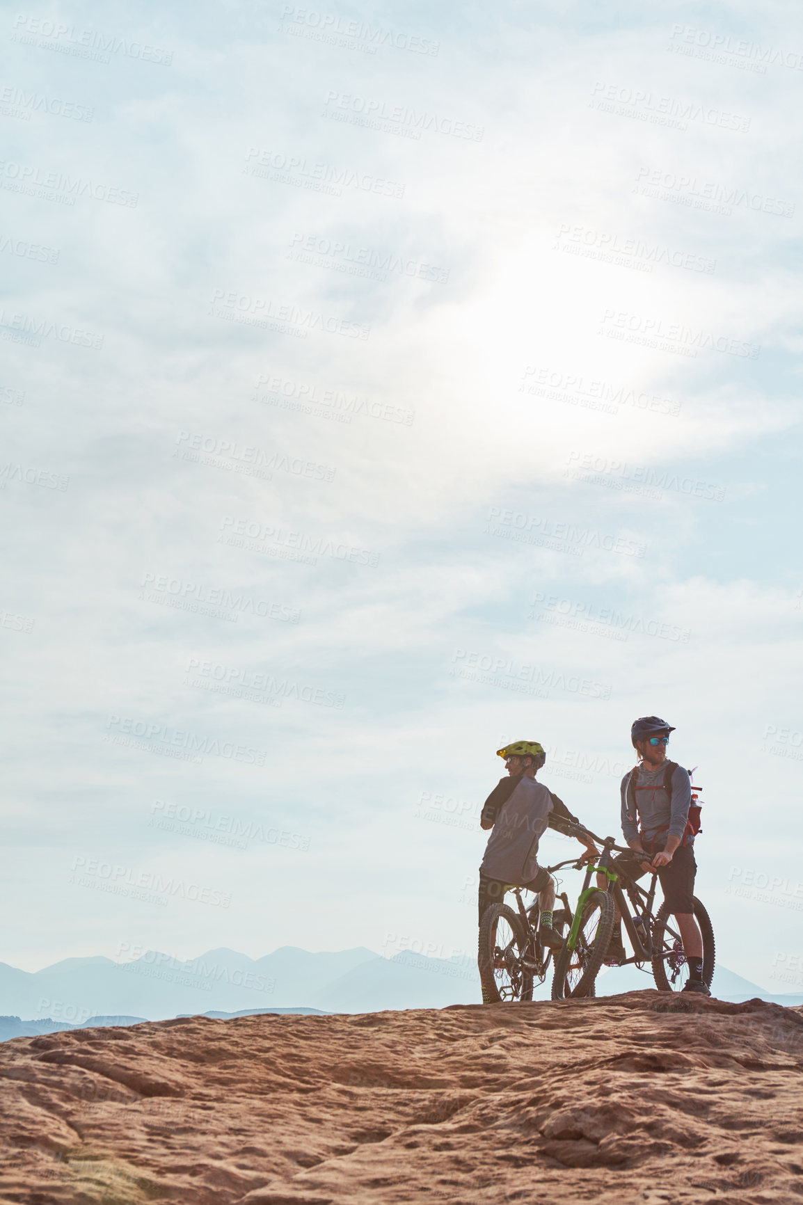 Buy stock photo Full length shot of two athletic men taking a break to admire the view while mountain biking through the wilderness