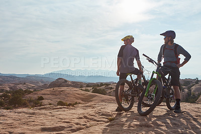 Buy stock photo Full length shot of two athletic men taking a break to admire the view while mountain biking through the wilderness