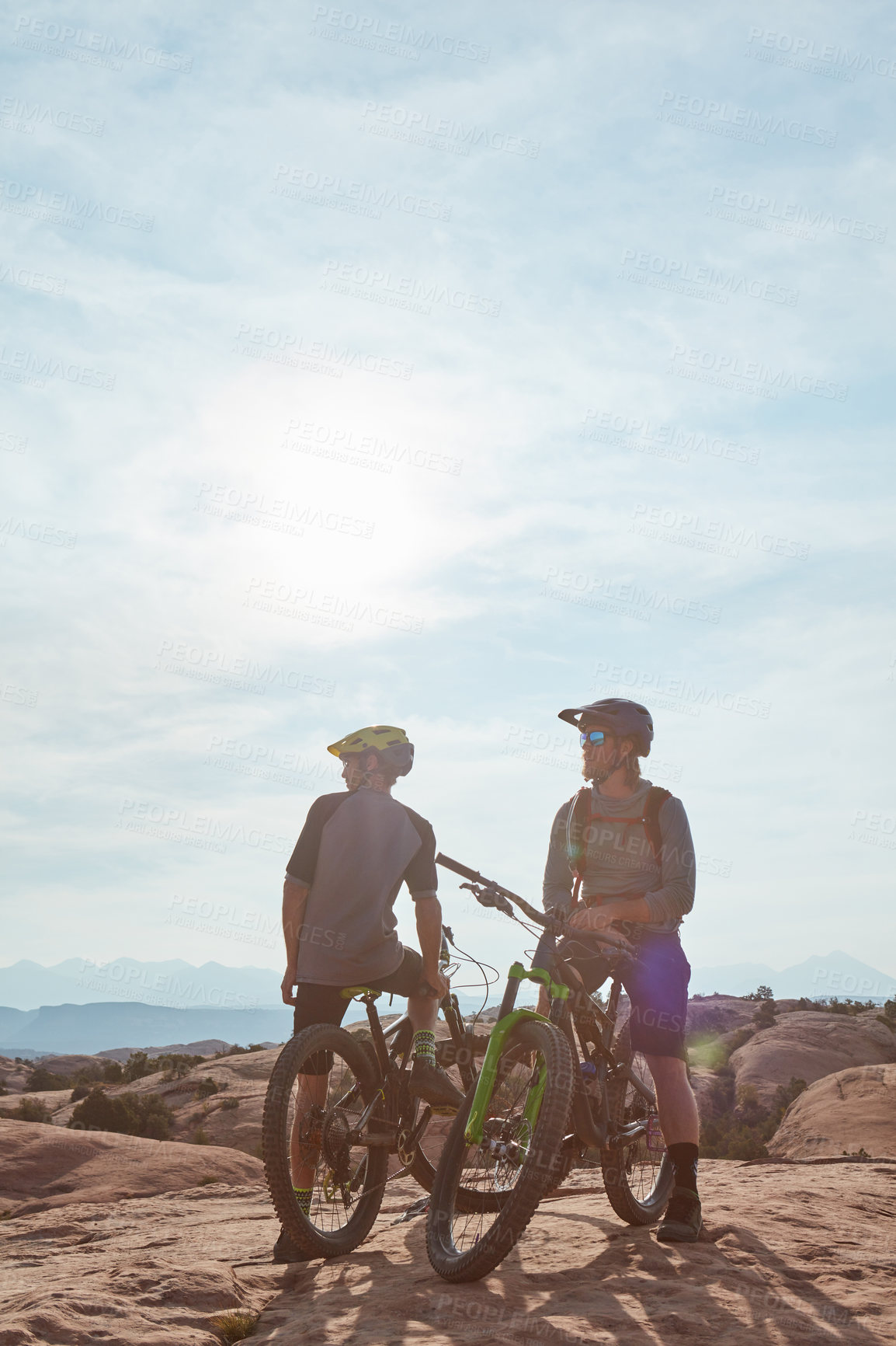 Buy stock photo Full length shot of two athletic men taking a break to admire the view while mountain biking through the wilderness