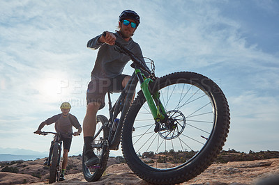 Buy stock photo Full length shot of two athletic men mountain biking through the wilderness