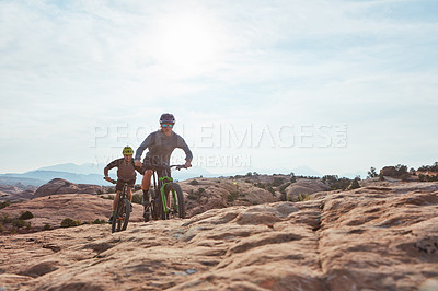 Buy stock photo Full length shot of two athletic men mountain biking through the wilderness