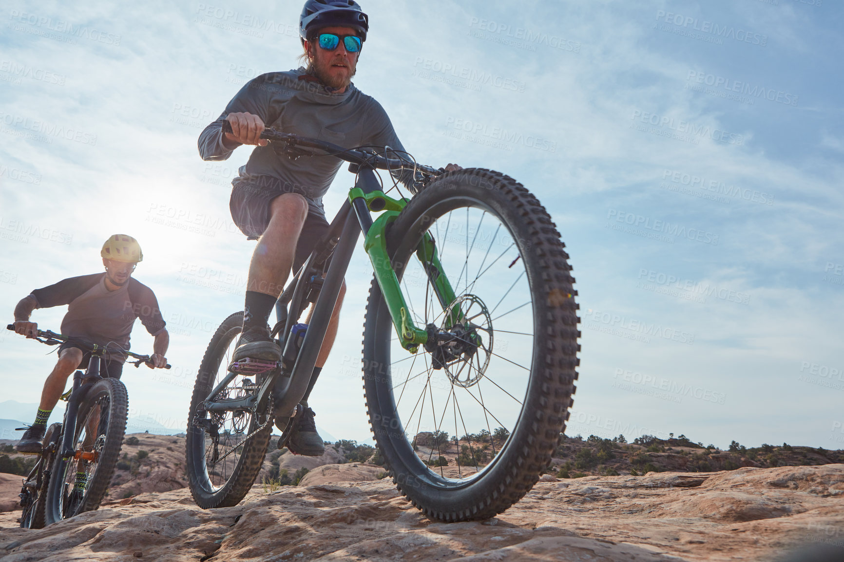 Buy stock photo Full length shot of two athletic men mountain biking through the wilderness