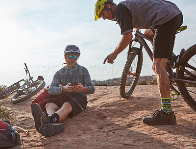 Buy stock photo Full length shot of two athletic men taking a break while mountain biking through the wilderness