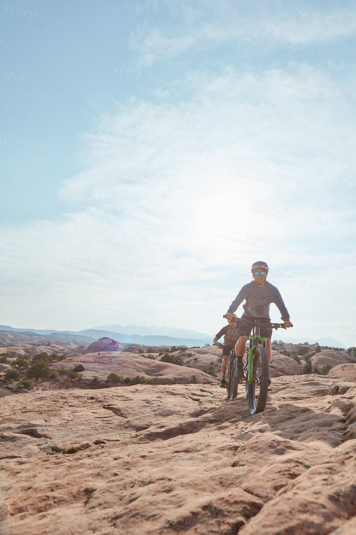 Buy stock photo Full length shot of two athletic men mountain biking through the wilderness