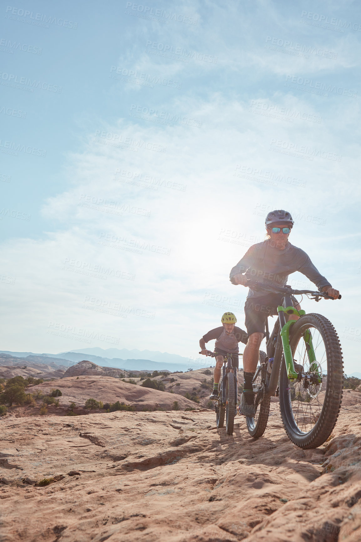 Buy stock photo Full length shot of two athletic men mountain biking through the wilderness