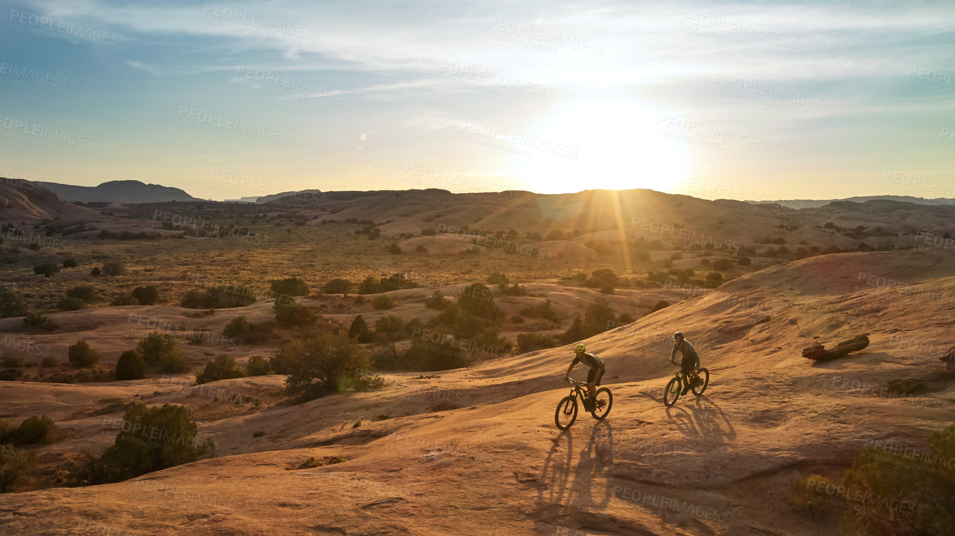 Buy stock photo Full length shot of two young male athletes mountain biking in the wilderness