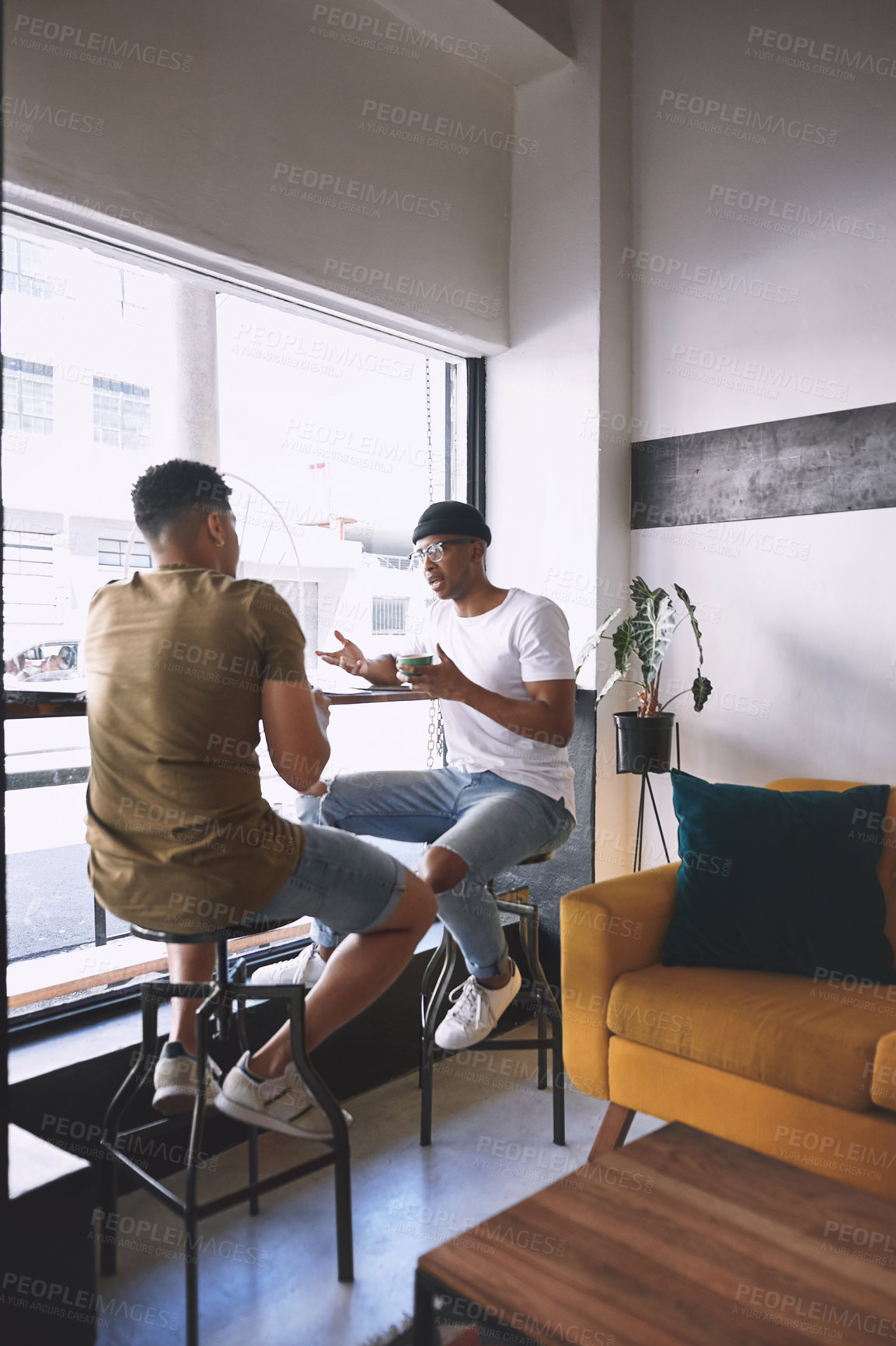 Buy stock photo Shot of two young men talking while having coffee together in a cafe