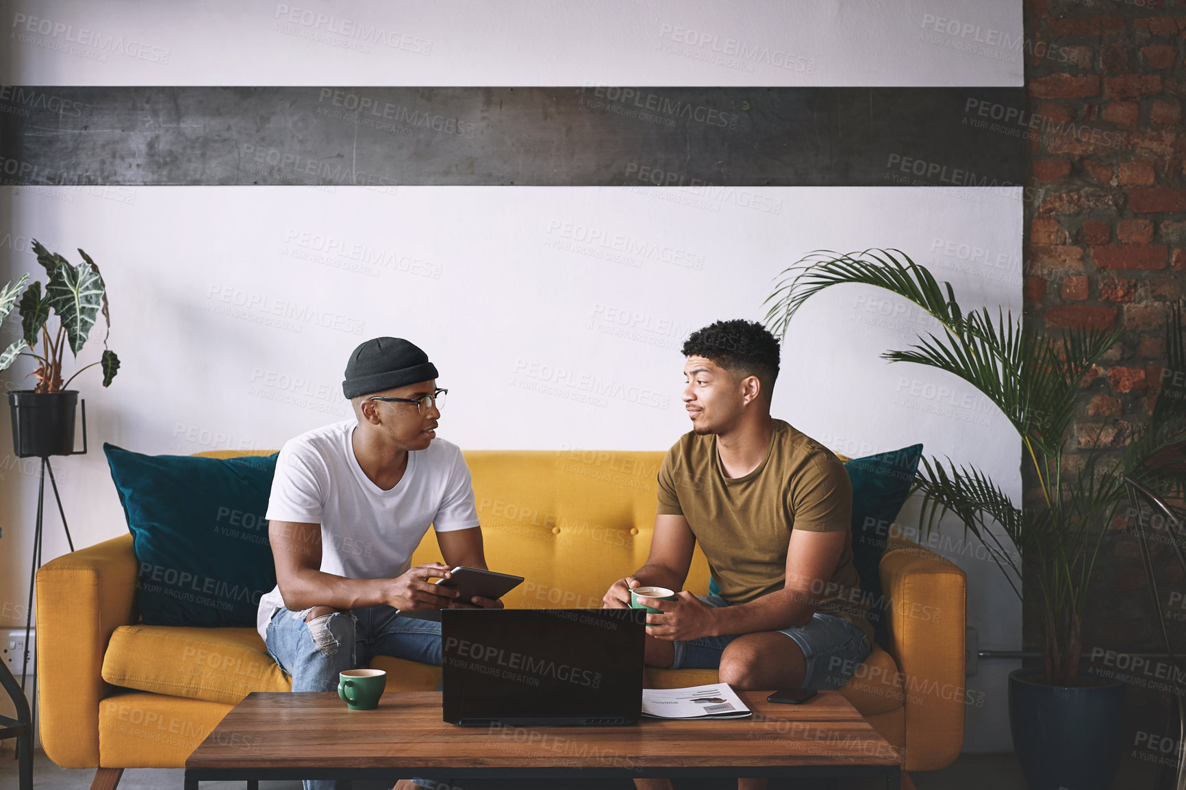 Buy stock photo Shot of two men using a laptop and a digital tablet while having coffee together