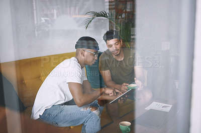 Buy stock photo Shot of two young men discussing something on a digital tablet while having coffee together