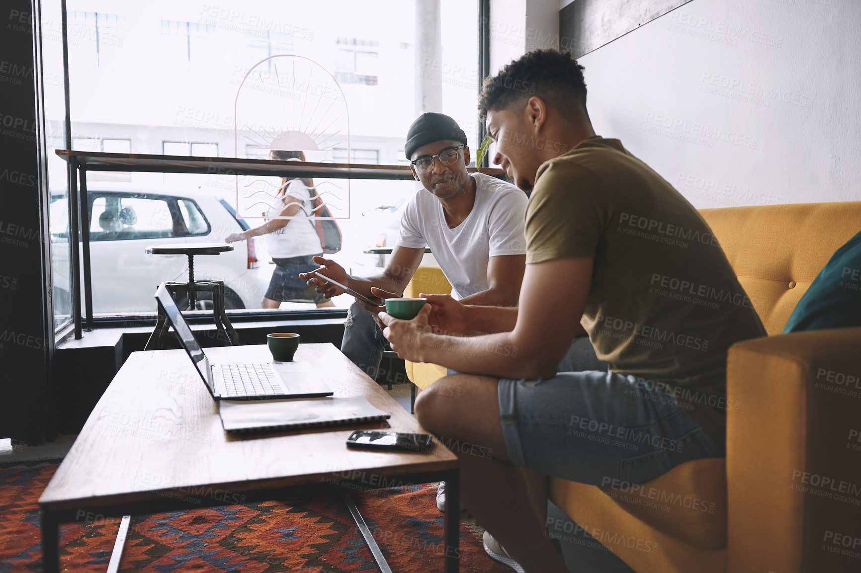 Buy stock photo Shot of two men using a laptop and a digital tablet while having coffee together