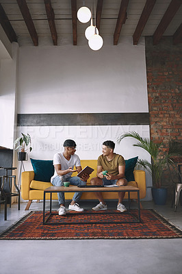 Buy stock photo Shot of two young men using a digital tablet while having coffee together
