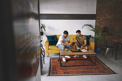 Buy stock photo Shot of two young men using a digital tablet while having coffee together