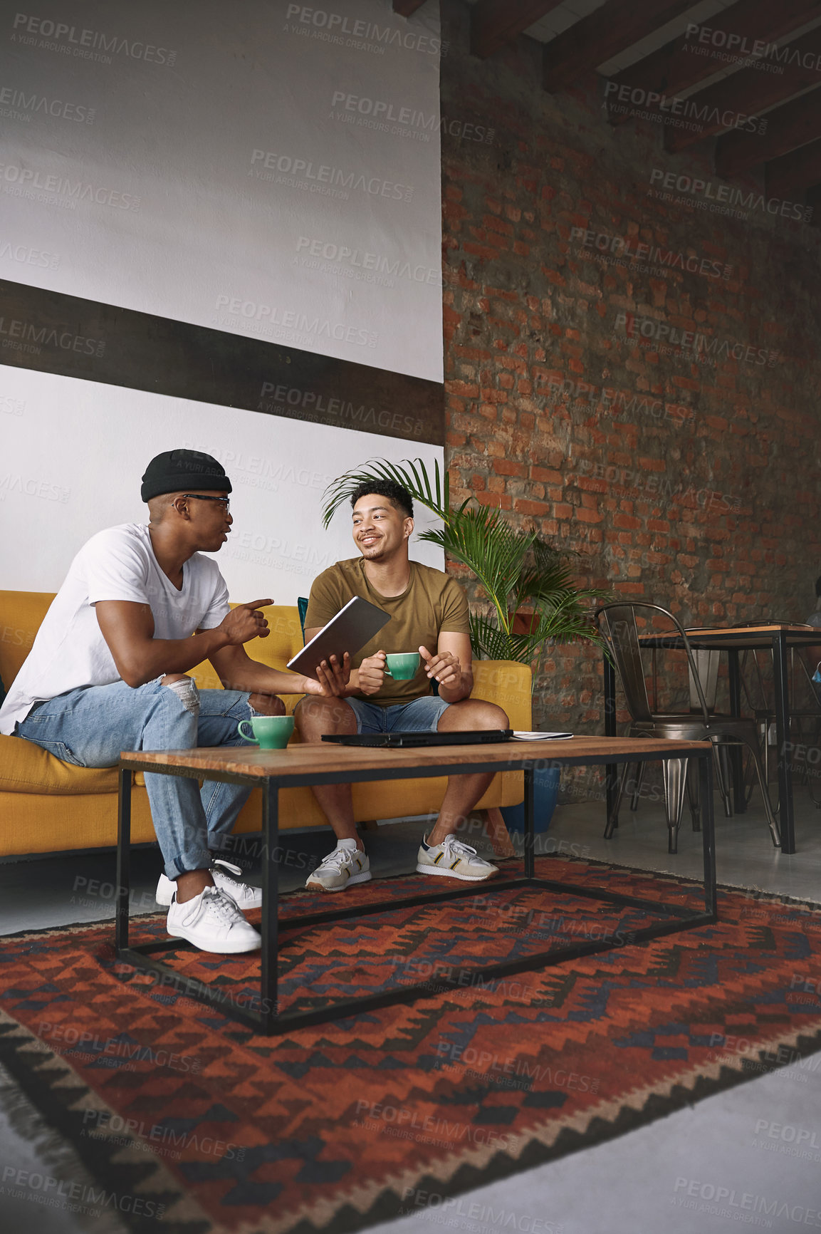 Buy stock photo Shot of two young men using a digital tablet while having coffee together