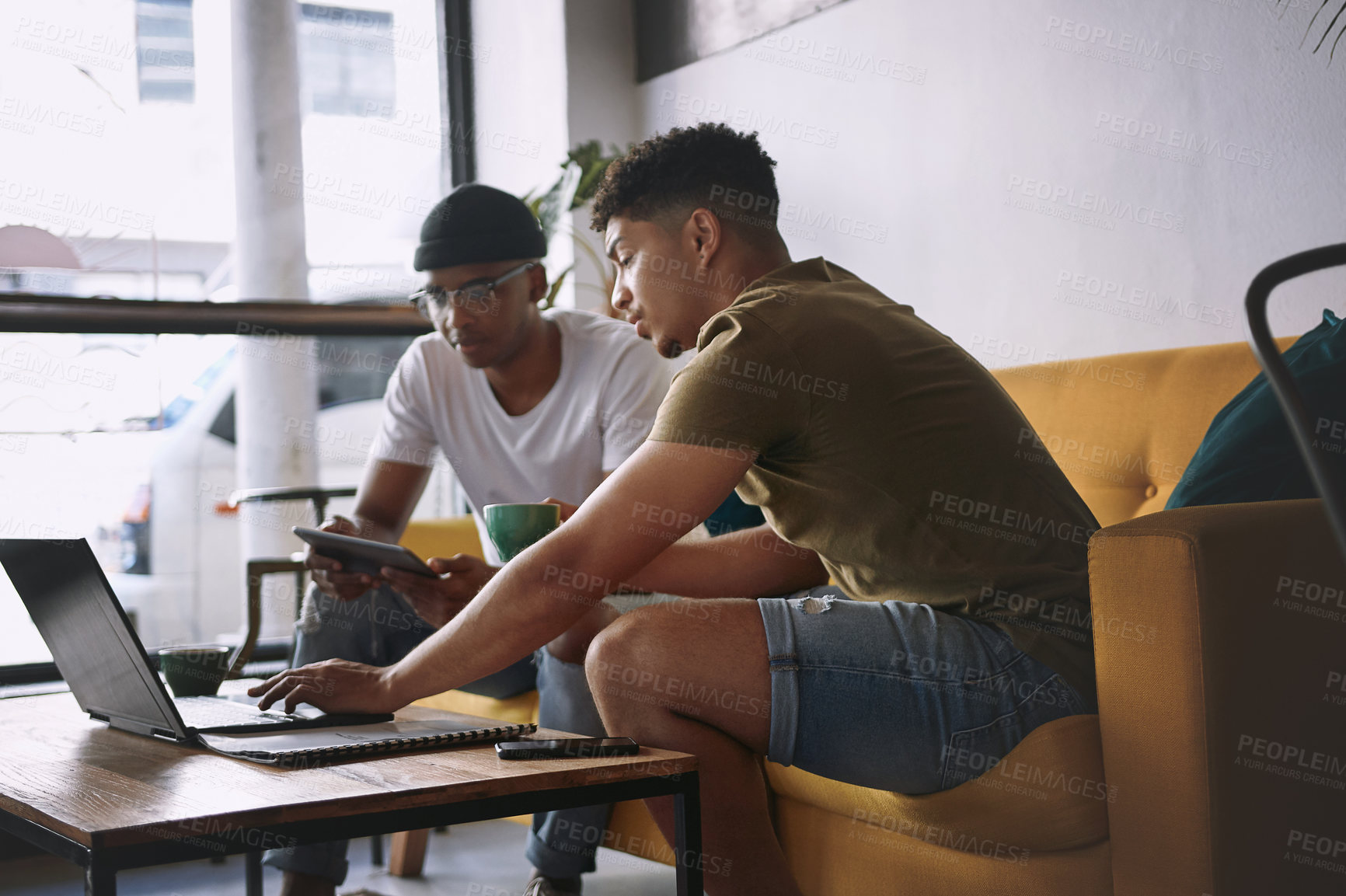 Buy stock photo Shot of two young men discussing something on a laptop while sitting together in a cafe