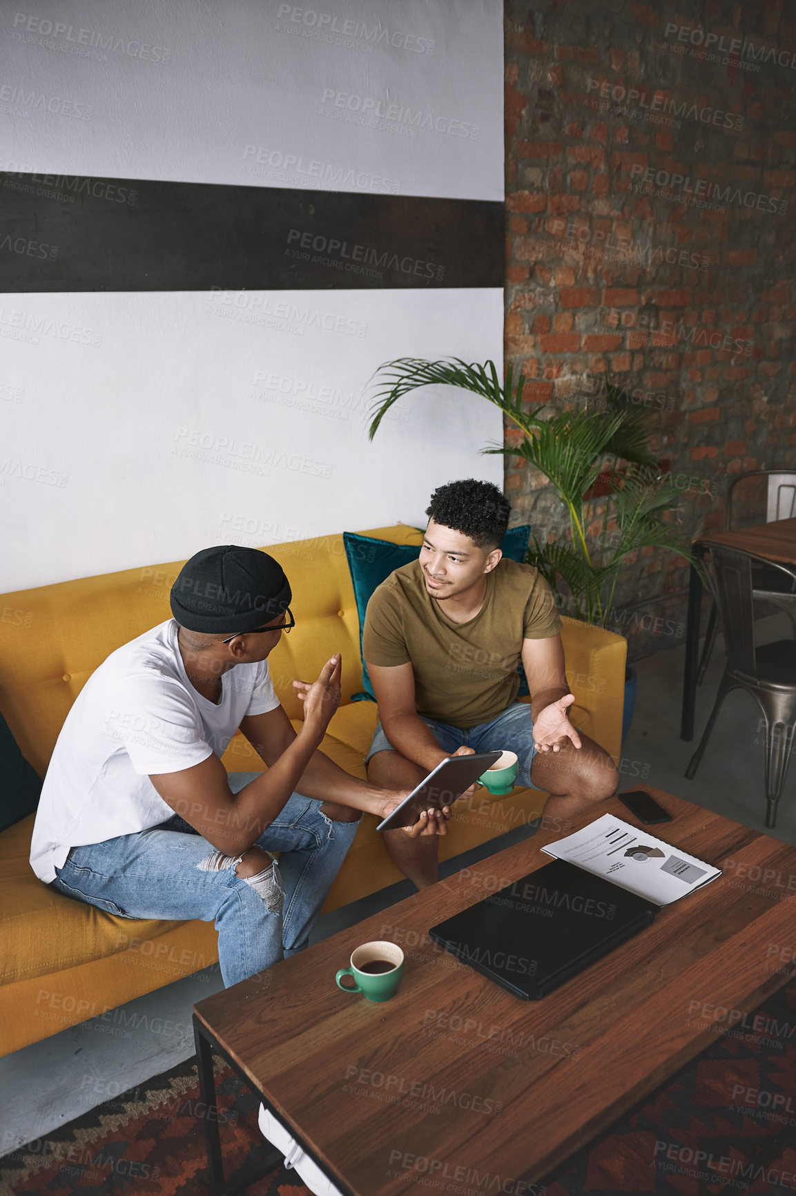 Buy stock photo Shot of two young men using a digital tablet while sitting together in a coffee shop