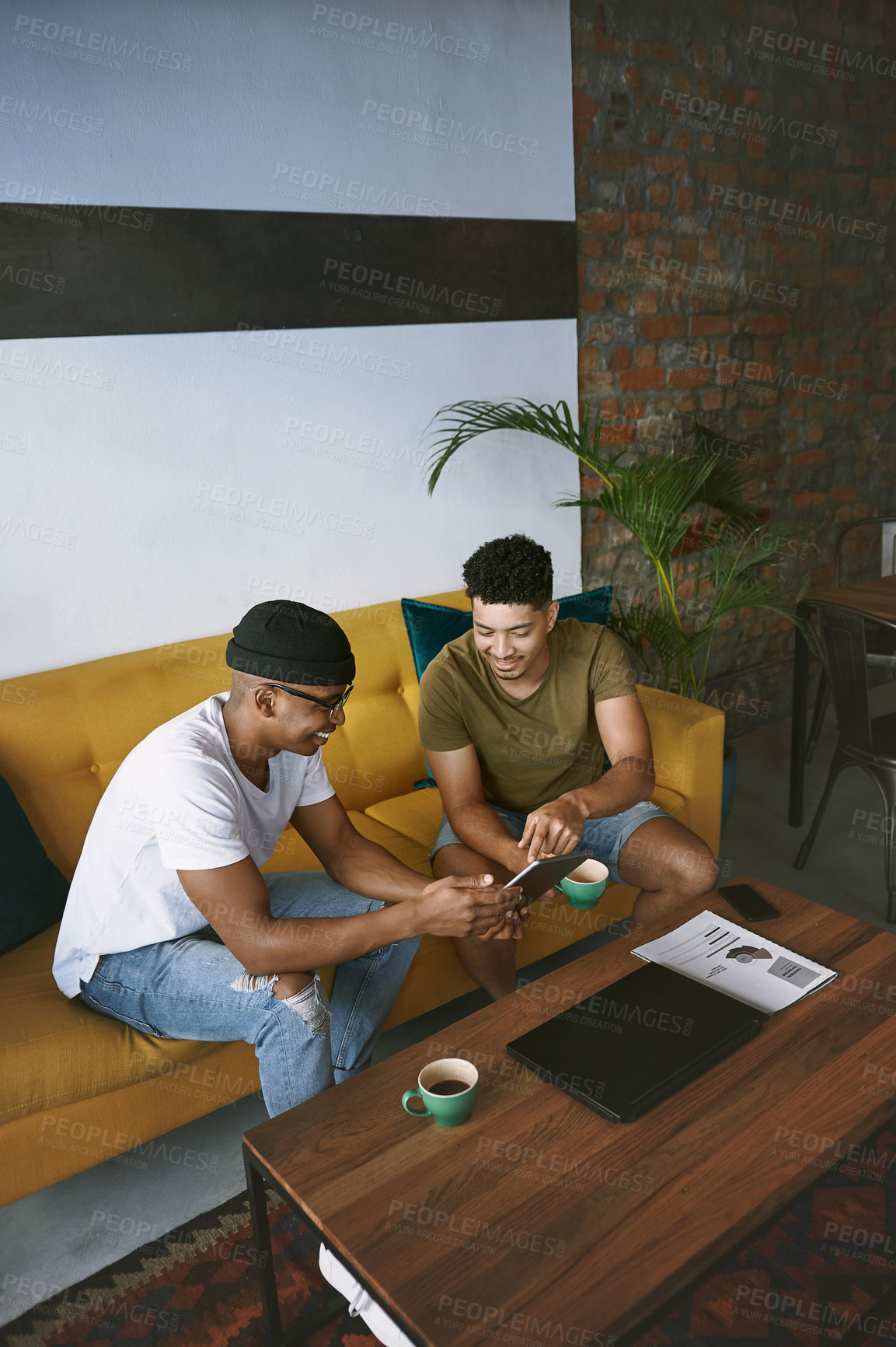 Buy stock photo Shot of two young men using a digital tablet while sitting together in a coffee shop