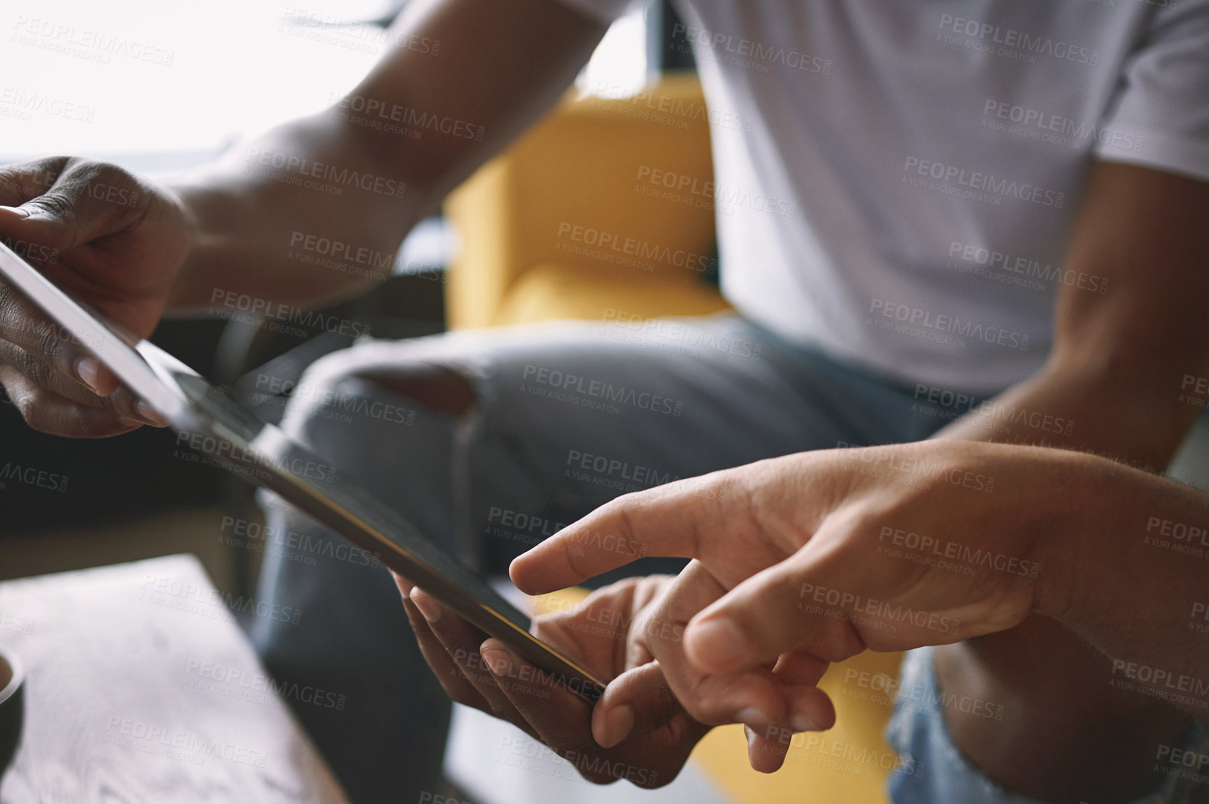 Buy stock photo Shot of two young men using a digital tablet while sitting together in a coffee shop