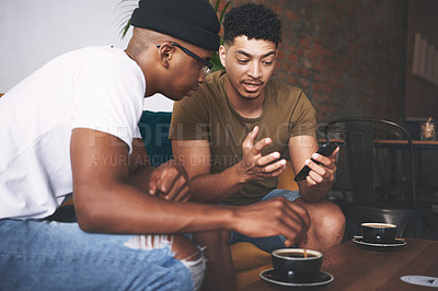 Buy stock photo Shot of men discussing something on a cellphone while sitting together in a coffee shop