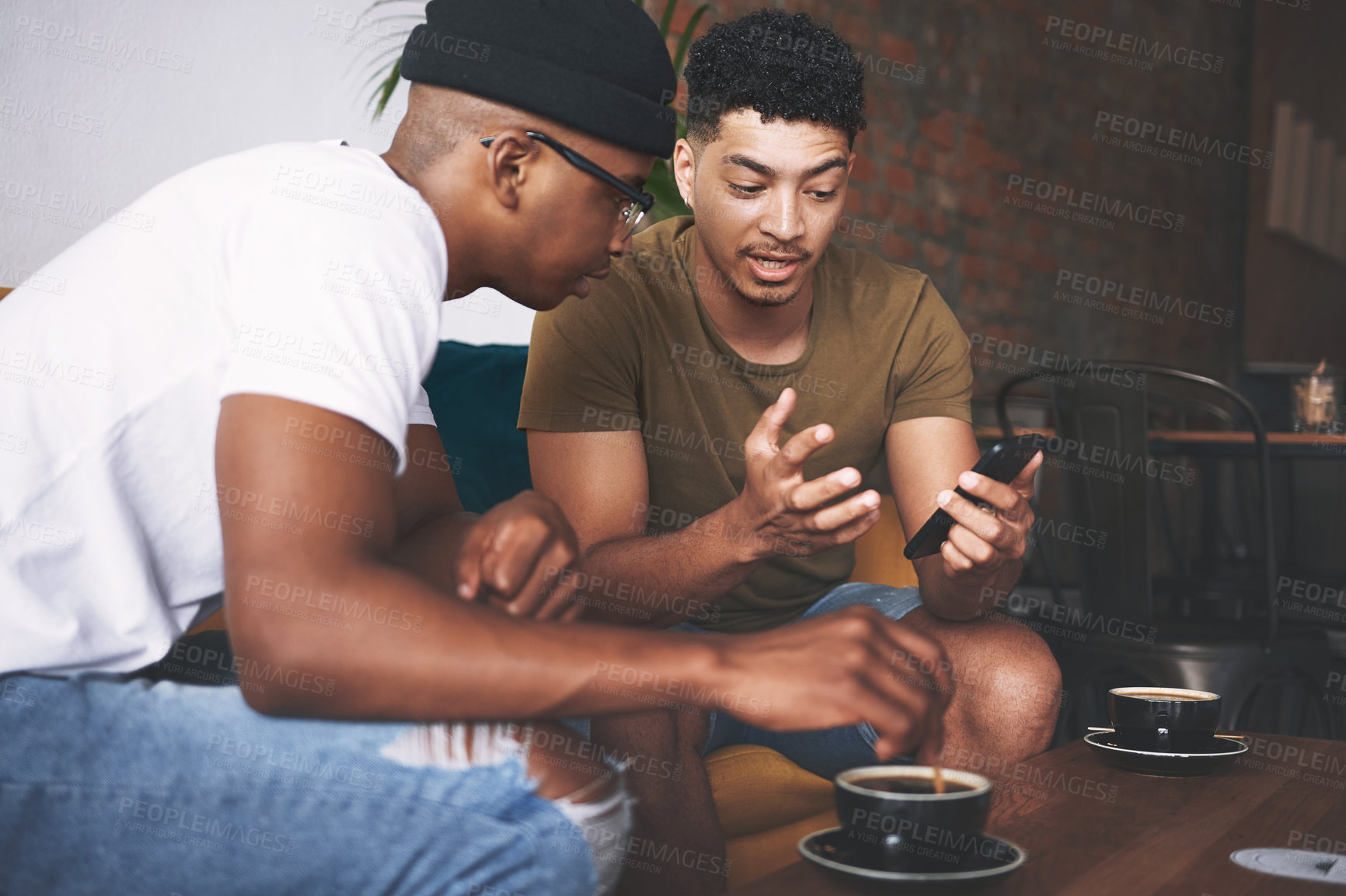 Buy stock photo Shot of men discussing something on a cellphone while sitting together in a coffee shop