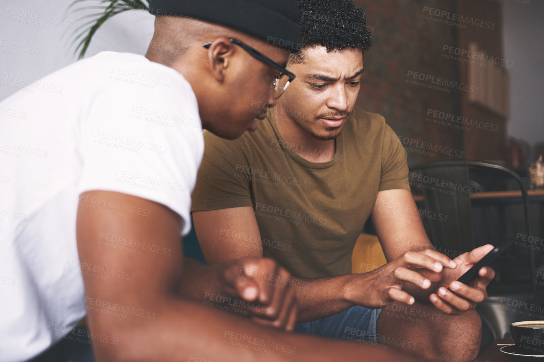 Buy stock photo Shot of men discussing something on a cellphone while sitting together in a coffee shop