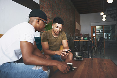 Buy stock photo Shot of men discussing something on a cellphone while sitting together in a coffee shop