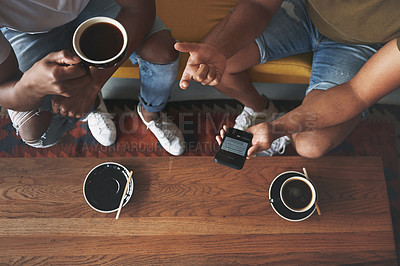 Buy stock photo Shot of men discussing something on a cellphone while sitting together in a coffee shop