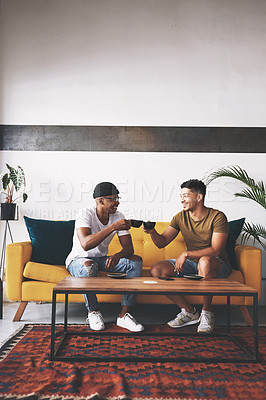 Buy stock photo Shot of two young men sharing a toast while sitting together in a coffee shop