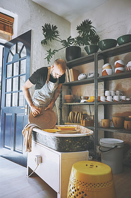 Buy stock photo Shot of a young man cleaning a pottery wheel in a ceramic studio
