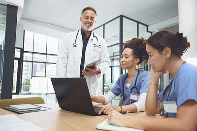 Buy stock photo Shot of a team of doctors using a laptop during a meeting in a hospital