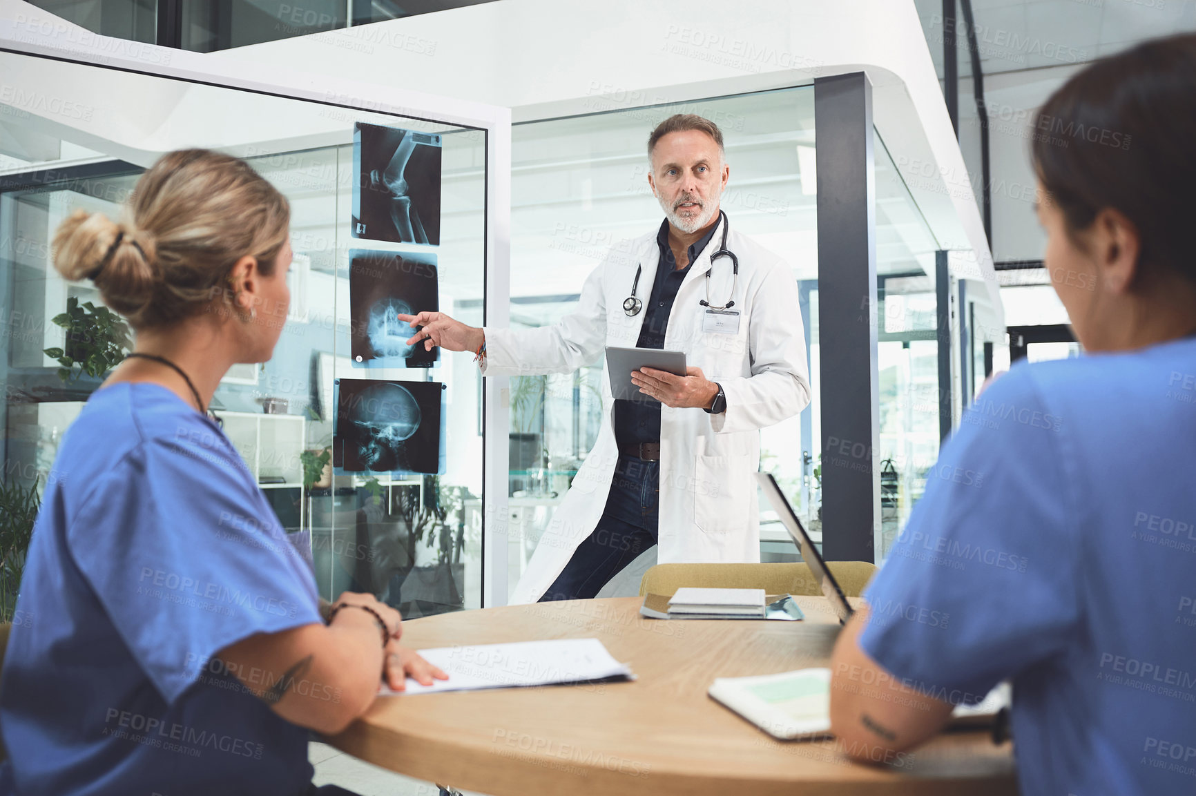 Buy stock photo Shot of a mature doctor analysing x-rays with his colleagues during a meeting in a hospital