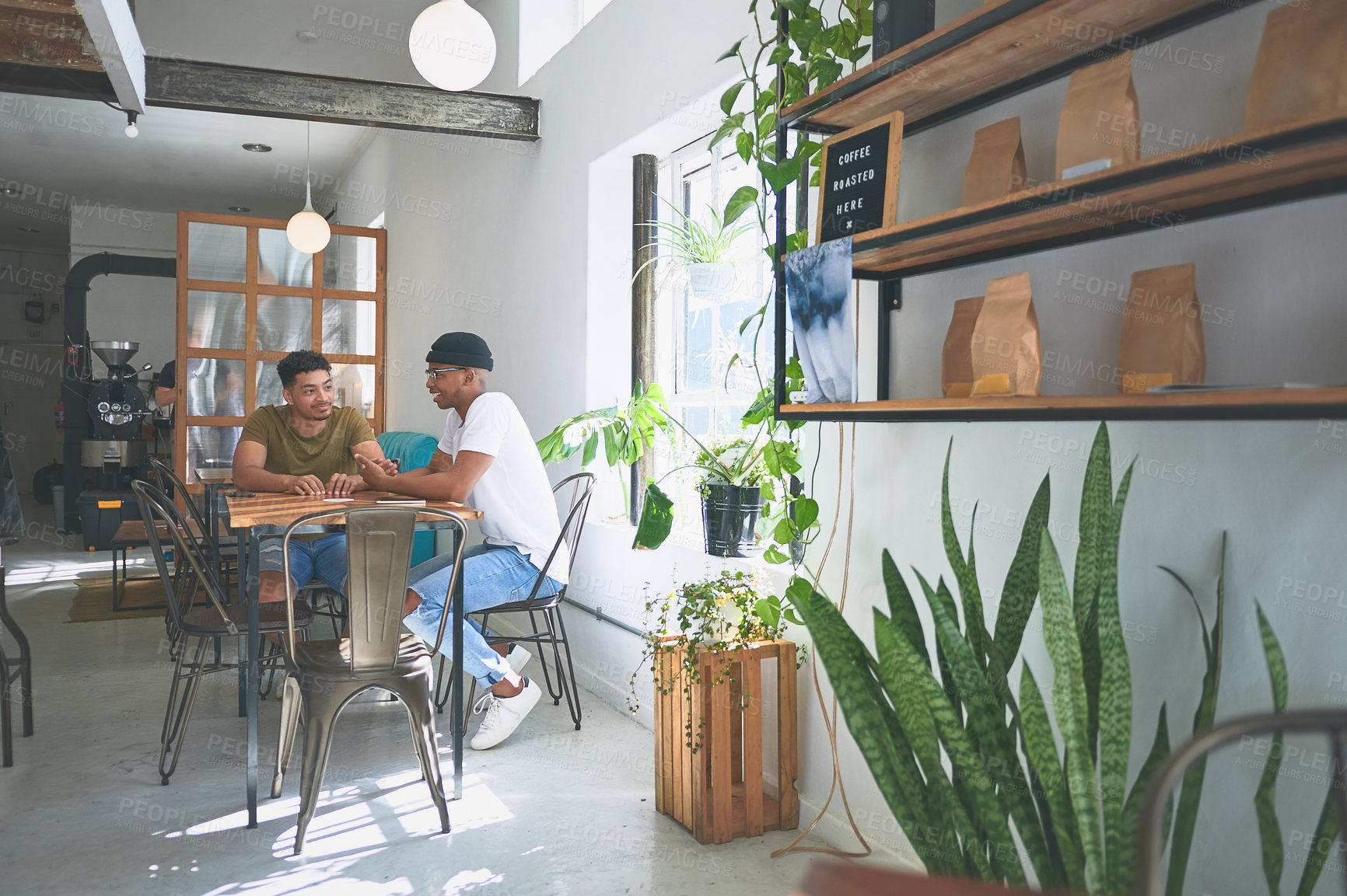 Buy stock photo Full length shot of two handsome friends sitting together and bonding in a coffeeshop during the day