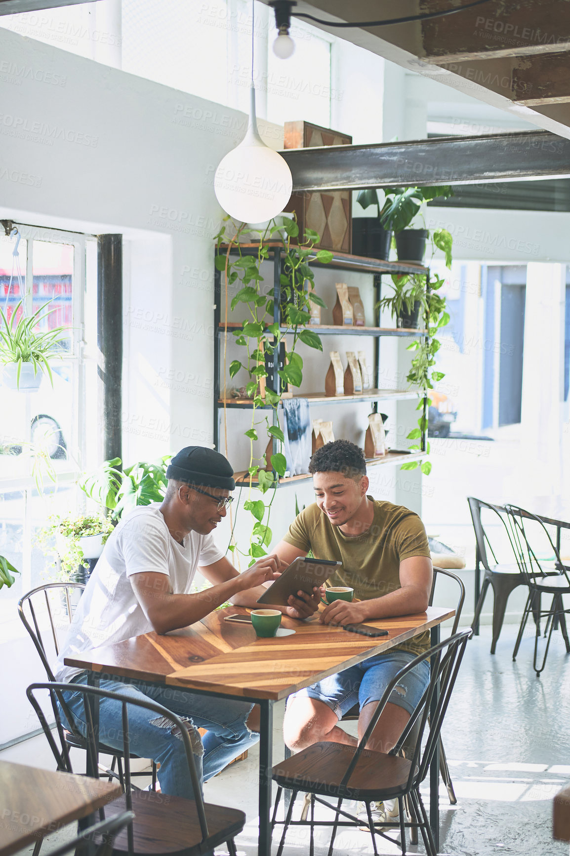 Buy stock photo Cropped shot of two handsome friends sitting together and bonding over a coffee in a cafe during the day