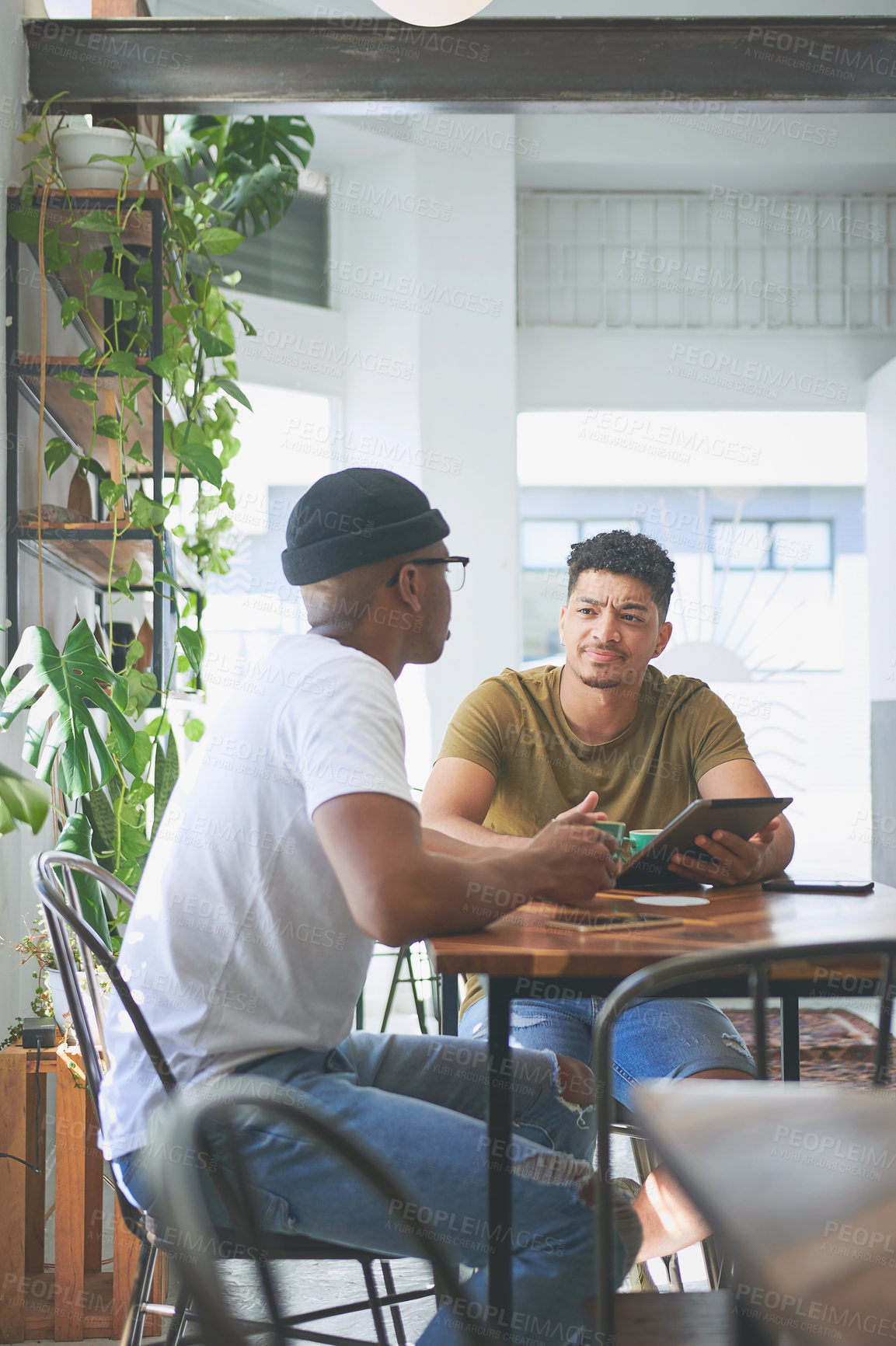 Buy stock photo Cropped shot of two handsome friends sitting together and using a tablet during a discussion in a coffeeshop