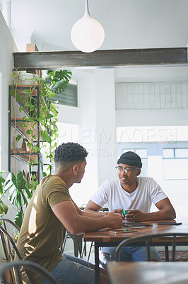 Buy stock photo Cropped shot of two handsome friends sitting together and having a discussion in a coffeeshop