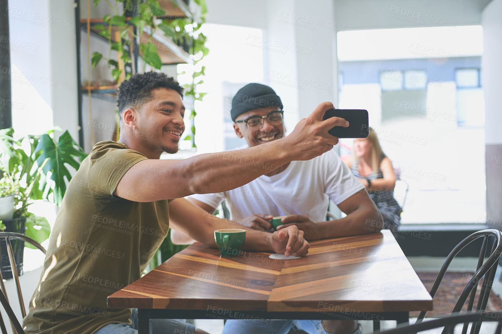 Buy stock photo Cropped shot of two handsome friends sitting together and using a cellphone to take a selfie in a coffeeshop