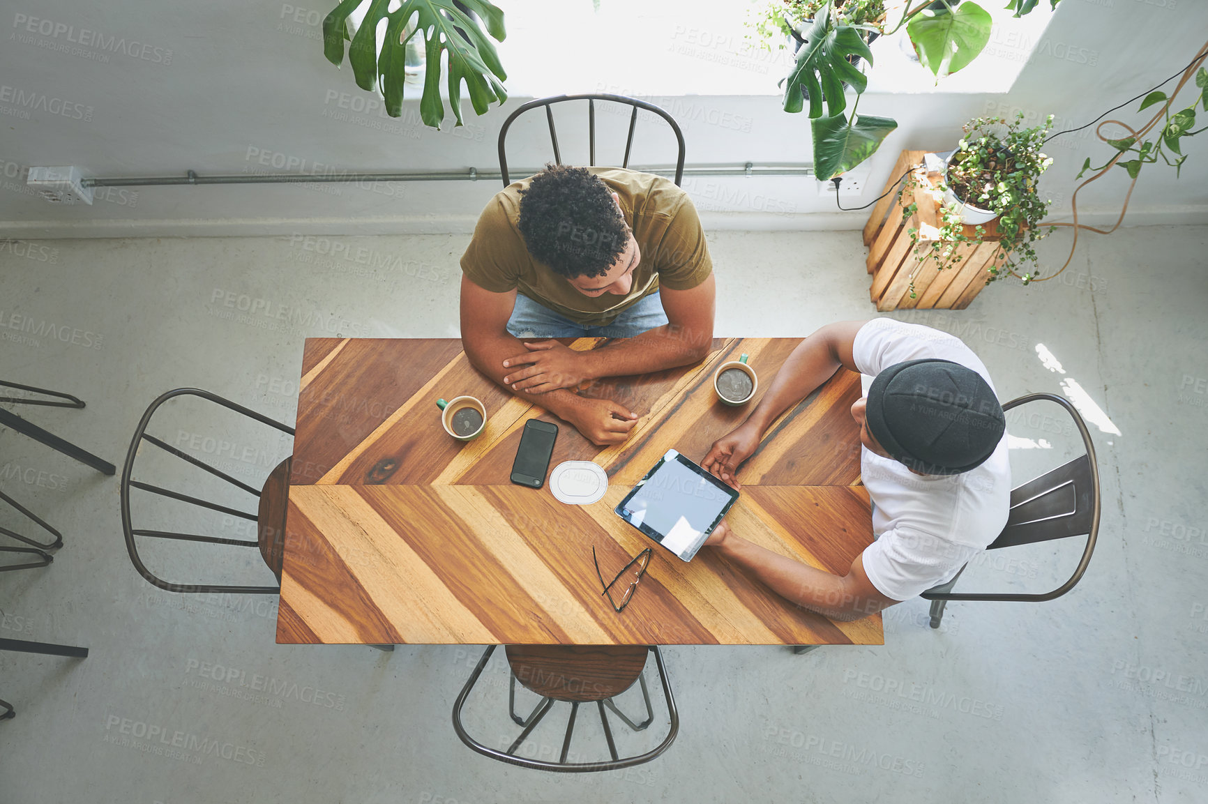 Buy stock photo High angle shot of two unrecognizable friends sitting together and using a tablet in a coffeeshop