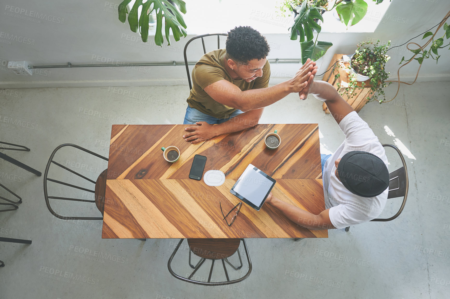 Buy stock photo High angle shot of two handsome friends sitting in a coffeeshop together and giving each other a high five