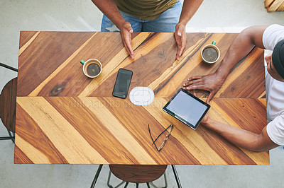 Buy stock photo High angle shot of two unrecognizable friends sitting together and using a tablet in a coffeeshop