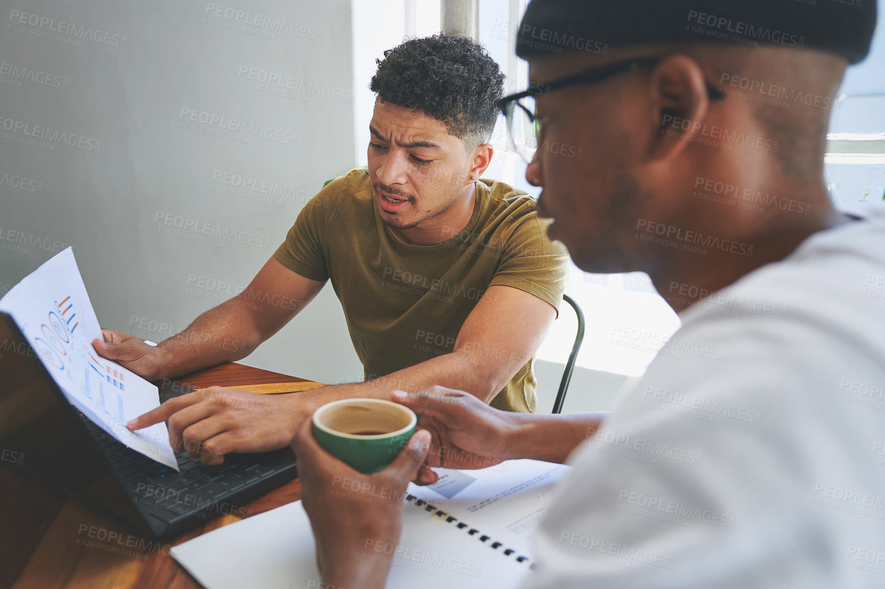 Buy stock photo Cropped shot of two handsome friends sitting together and reading through paperwork in a coffeeshop