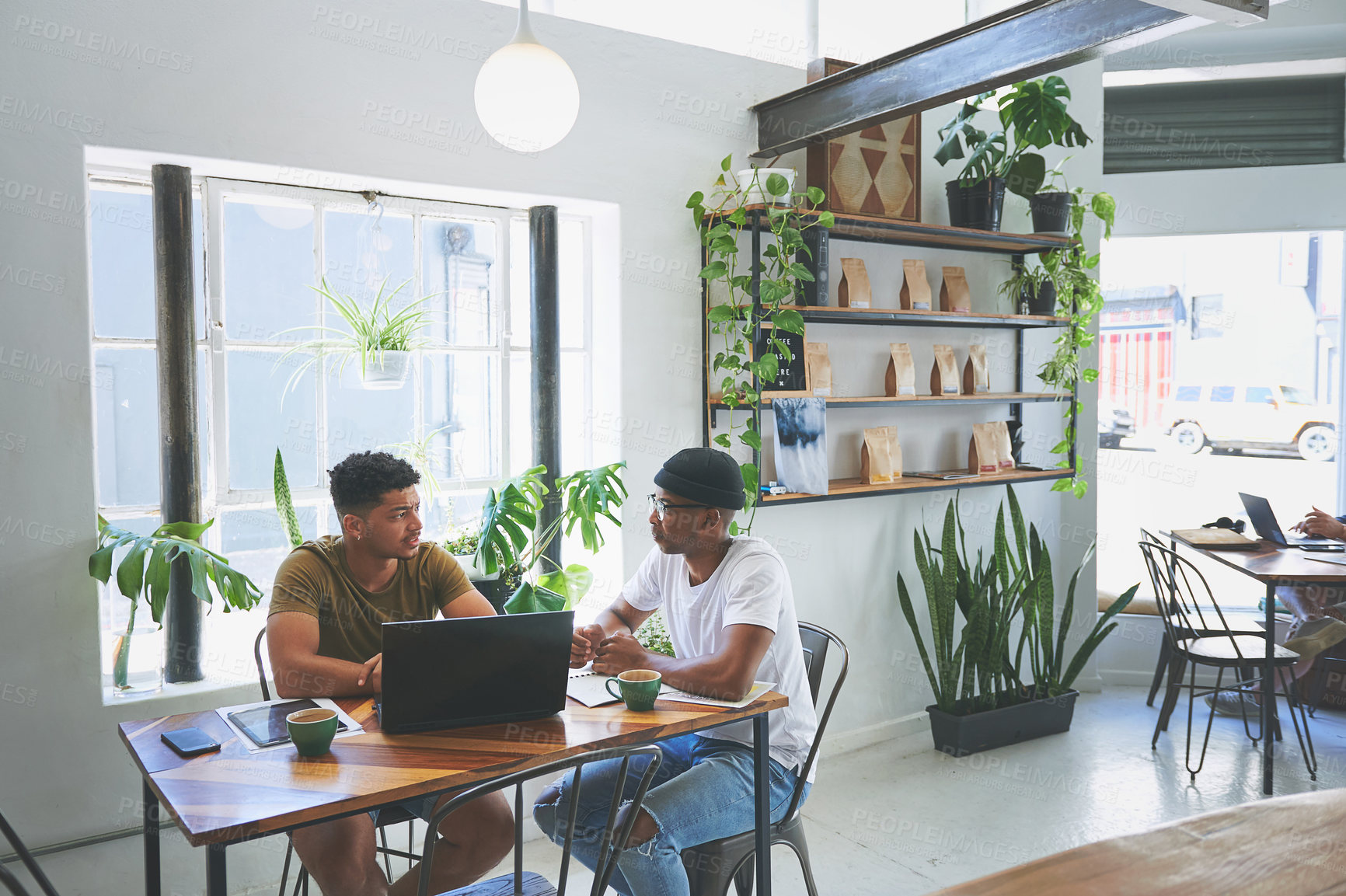 Buy stock photo Cropped shot of two handsome friends sitting together in a coffeeshop and having a discussion