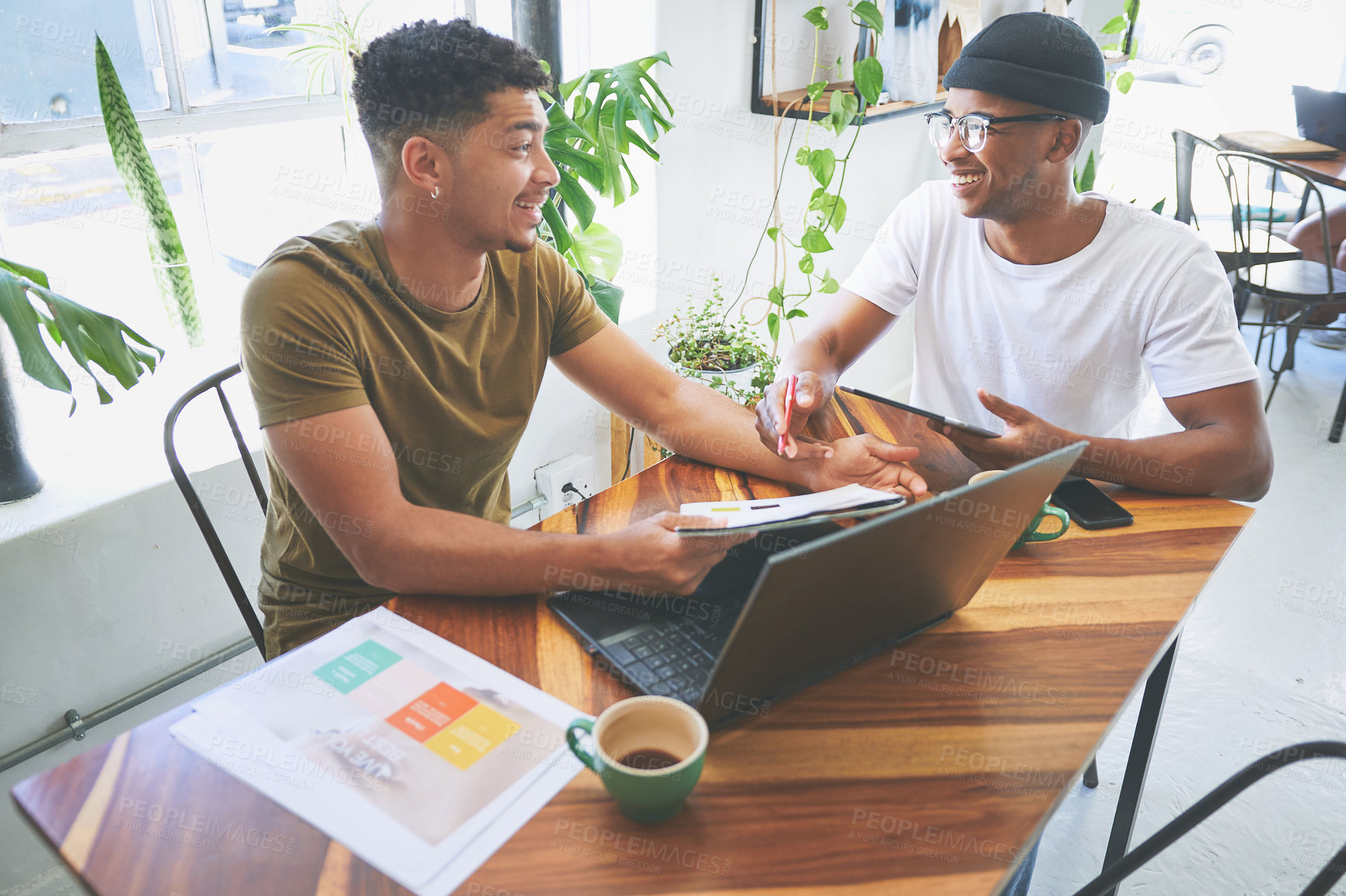 Buy stock photo Cropped shot of two handsome friends sitting together in a coffeeshop and reading through paperwork during a discussion