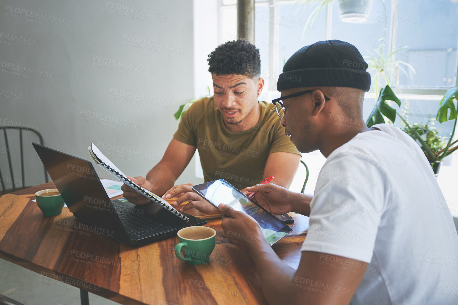 Buy stock photo Cropped shot of two handsome friends sitting together and reading through paperwork in a coffeeshop